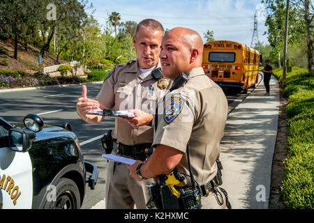 Uniformierte Hispanic und kaukasischen Polizisten beobachten road Bedingungen, die zu einer Schule Busunglueck in Laguna Hills, CA. Beachten Sie Bus und Fahrer im Hintergrund. Stockfoto