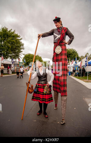 Das Tragen eines bunten Tartan, ein Schotte mit Motorhaube und Kilt auf Stelzen erhält einige Bewunderung von einem kostümierte Dame an einem schottischen Festival in Costa Mesa, CA. Stockfoto