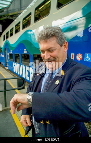Ein zugschaffner in der King Street Station in Seattle, WA, prüft seine Uhr vor Signalisierung Abfahrtszeit für einen Nachmittag trainieren. Stockfoto