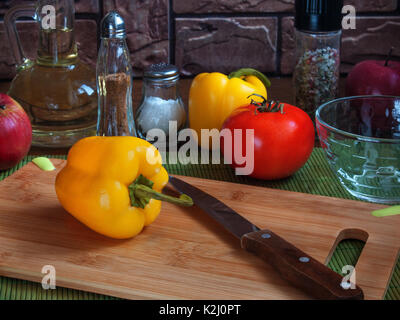 Große saftige gelbe Paprika auf einem hölzernen Schneidebrett auf einem Tisch mit roten Tomaten, Äpfel, Pflanzenöl, Salz, Gewürze Stockfoto