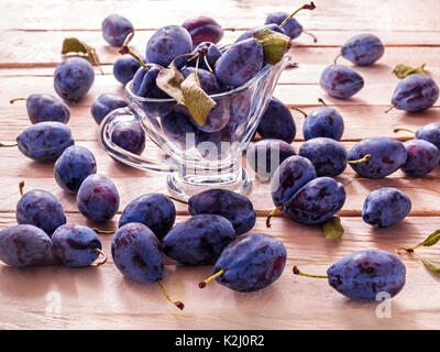 Blau große Pflaumen saftige süße Frucht für diätetische Ernährung liegen in einem Glas Becher auf eine Planke Hintergrund Stockfoto