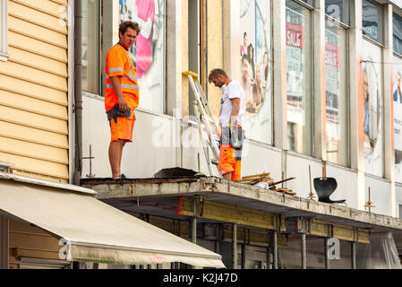 Kristiansand, Norwegen - 16. August 2017: Reisedokumentation Bauarbeiter arbeiten an der Renovierung des Daches Regal über der Straße. Stockfoto