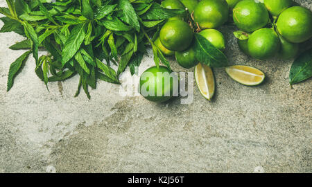 Frisch gepflückte organische Limes und Minze für die Cocktail oder Limonade über grauer Beton Stein, Ansicht von oben, Kopieren, horizontale compositio Stockfoto