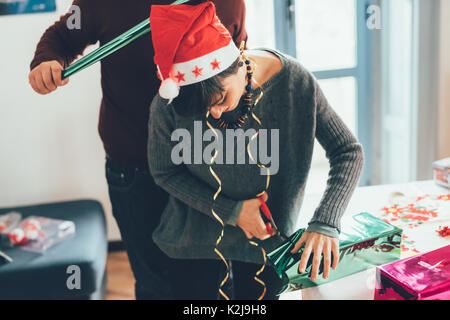 Knie Abbildung der Jungen stattlichen kaukasischen Mann und Frau paar Verpacken Weihnachten mit Verpackung Papier und Farbband vorhanden, sowohl nach unten schauen - Christus Stockfoto