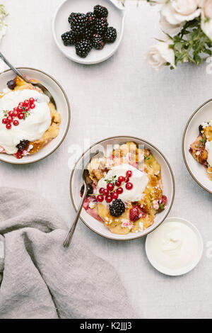 Ein Ziegenkäse & Berry Brotpudding wird aus der Sicht von oben fotografiert, nachdem es in Schalen gelegt wurde und abgerundet mit Creme fraiche und roten Johannisbeeren. Stockfoto