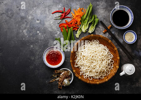 Raw Udon Nudeln in Bambus Korb und Zutaten zum Kochen asiatische Lebensmittel mit Tiger Garnelen, Grüns, Gemüse, Gewürze auf dunklem Hintergrund Kopie Raum Stockfoto