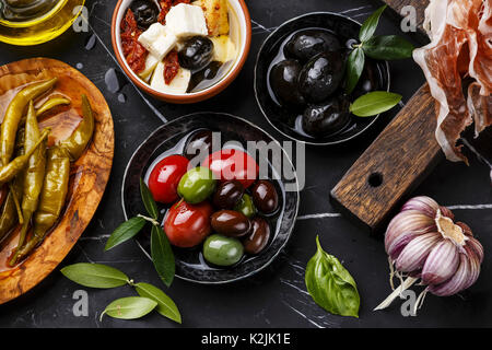 Italienische Snacks essen mit Oliven, Feta Käse mit getrockneten Tomaten, Schinken, Knoblauch, Basilikum und Peperoni Pfeffer auf dunklem Marmor Hintergrund close-up Stockfoto