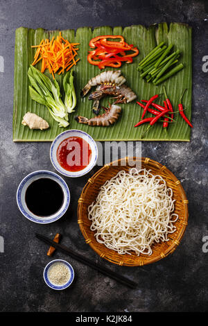 Zutaten zum Kochen Udon Nudeln mit Tiger Garnelen, grünen, Gemüse, Gewürze auf bananenblatt auf dunklem Hintergrund Stockfoto