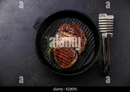 Gegrilltes Rib Eye Steak und Zange auf Grillpfanne auf dunklem Hintergrund Stockfoto
