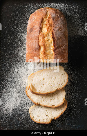 In Scheiben geschnitten weißen hausgemachte Brot aus Weizen mit Weizen Mehl auf alten schwarzen Backblech als Hintergrund. Ansicht von oben Stockfoto