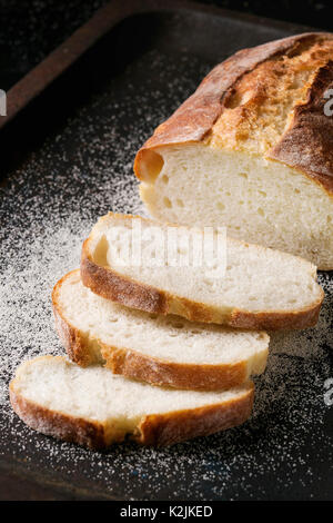 In Scheiben geschnitten weißen hausgemachte Brot aus Weizen mit Weizen Mehl auf alten schwarzen Backblech als Hintergrund. Nahaufnahme Stockfoto