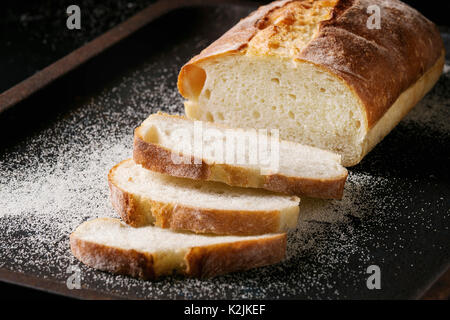 In Scheiben geschnitten weißen hausgemachte Brot aus Weizen mit Weizen Mehl auf alten schwarzen Backblech als Hintergrund. Nahaufnahme Stockfoto