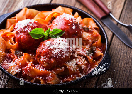 Hausgemachte, traditionelle italienische Nudeln Pappardelle mit Frikadellen und Basilikum Kraut serviert mit Käse Grana Padana auf rustikalen Holztisch Stockfoto