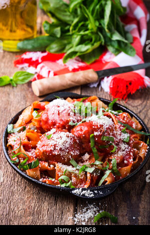 Hausgemachte, traditionelle italienische Nudeln Pappardelle mit Frikadellen und Basilikum Kraut serviert mit Käse Grana Padana in Gusseisen Skillet auf rustikalen Holzmöbeln ta Stockfoto