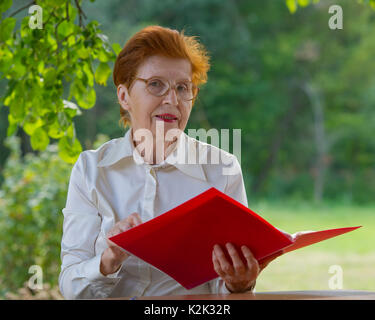 Eine Frau der eine Geschäftsfrau im Alter schaut auf Dokumente. Alter 80 Jahre. Porträt einer Frau, die Brille im Freien. Stockfoto