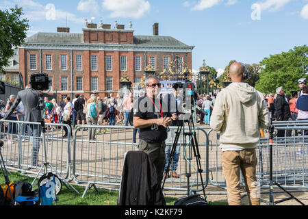 Ein Nachrichten Reporter und Kameramann mit einem Stück zu Kamera vor den Toren des Kensington Palace. Erinnerung an Prinzessin Diana, 20 Jahre nach ihrem Tod. Stockfoto