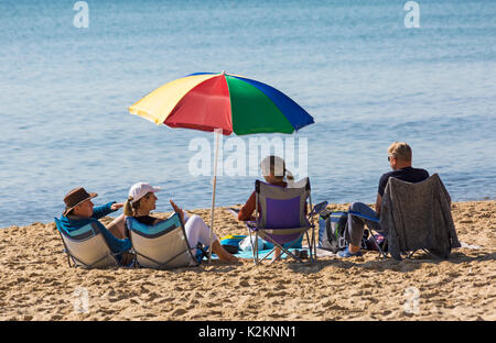 Bournemouth, Dorset, Großbritannien. September 2017. UK Wetter: Schöner warmer sonniger Tag am Bournemouth Strand an der Südküste. Strandgänger sitzen in Stühlen unter einem bunten Sonnenschirm. Quelle: Carolyn Jenkins/Alamy Live News Stockfoto