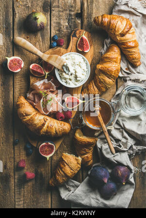 Frühstück mit frisch gebackenen Croissants, Ricotta, Feigen, frische Beeren, Prosciutto di Parma und Honig im Glas über rustikal Hintergrund Stockfoto