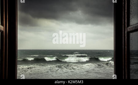 Dramatische Meerblick vom geöffneten Fenster mit großen stürmischen Wellen und dramatischen Himmel während Regen und Sturm Wetter im Herbst Jahreszeit am Meer Stockfoto