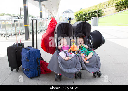 Fliegen mit zwei Mädchen im Doppelbuggy am Flughafen, London Stansted Stockfoto