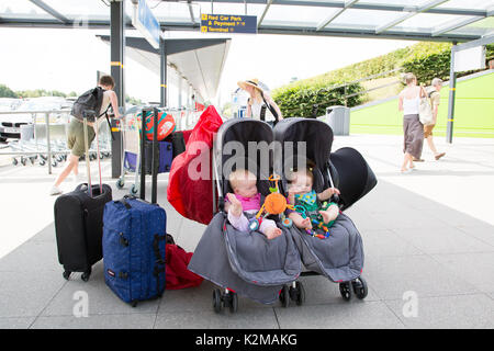 Fliegen mit zwei Mädchen im Doppelbuggy am Flughafen, London Stansted Stockfoto