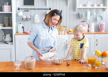 Mutter und Sohn lächelnd, während sie das Frühstück in der Küche. Mom gießt Milch und Cornflakes in Glas Stockfoto