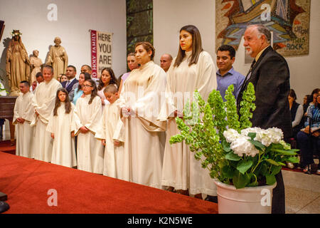 Multirassischen taufe Kandidaten und deren Sponsoren Line up neben den Altar bei einer Taufe Masse in einem Orange, CA, Katholische Kathedrale. Hinweis taufe Roben und Alter. Stockfoto