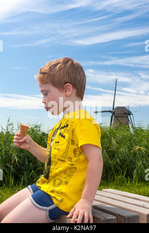 Ein Junge essen ein Eis mit einem traditionellen holländischen Windmühle im Hintergrund. Kinderdijk, Niederlande Stockfoto