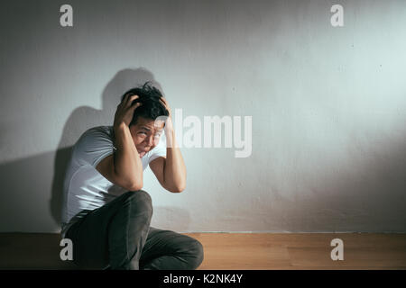 Autistischen geistige Behinderung Konzept der verrückt Angst Mann, Krankheit des Gehirns sitzt auf Holzboden allein Gefühl schrecklich in Dunkel mit Wh Stockfoto