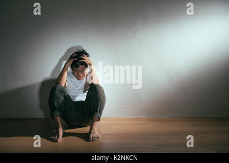 Junge Menschen mit autistischen Behinderungen Problem sitzen auf Holzboden wütend verrückt in dunklen Denken mit weißen Hintergrund. Stockfoto