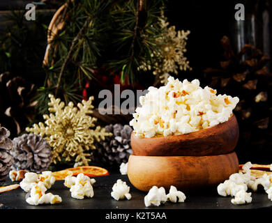 Popcorn in eine hölzerne Platte auf dem Hintergrund der Weihnachtsbäume und Weihnachtsschmuck, Neues Jahr bieten, selektiver Fokus Stockfoto