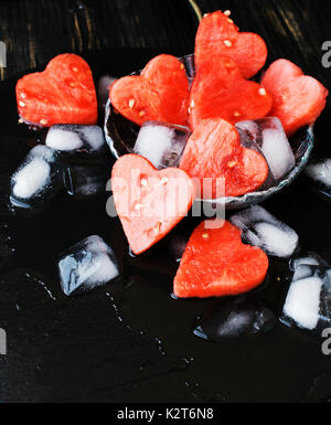 Wassermelone Herzen mit Eiswürfel auf schwarzen Stein Hintergrund für Valentinstag, selektiver Fokus, Platz für Text Stockfoto