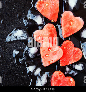 Wassermelone Herzen mit Eiswürfel auf schwarzen Stein Hintergrund für Valentinstag, selektiver Fokus, Platz für Text Stockfoto