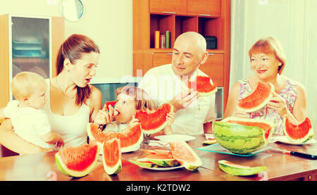 Glücklich drei Generationen Familie Essen Wassermelone über Tisch im Wohngebäude Stockfoto
