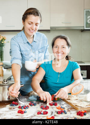 Lächelnde Frauen, die süßen Kuchen mit Beeren zusammen zu Hause Küche Stockfoto