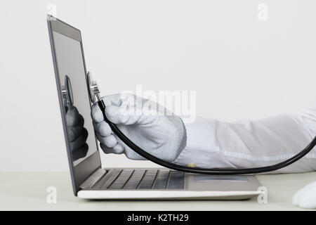 Nahaufnahme der Person Hände In weißen Handschuh prüfen Laptop mit Stethoskop Stockfoto