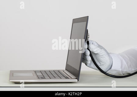 Nahaufnahme der Person Hände In weißen Handschuh prüfen Laptop mit Stethoskop Stockfoto