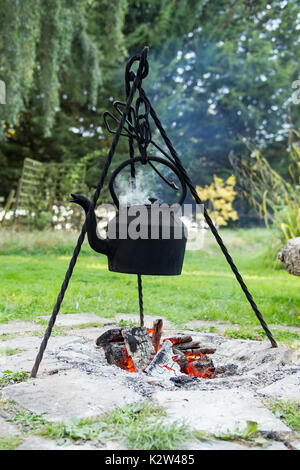 Eine geschwärzte Wasserkocher hängt an einem Stativ über einem offenen Feuer Stockfoto
