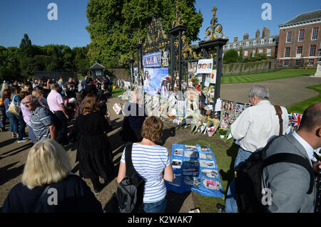 Leute schauen auf Blumen und Würdigungen zum 20. Jahrestag des Todes von Diana, Prinzessin von Wales, außerhalb der Kensington Palace, London. Stockfoto