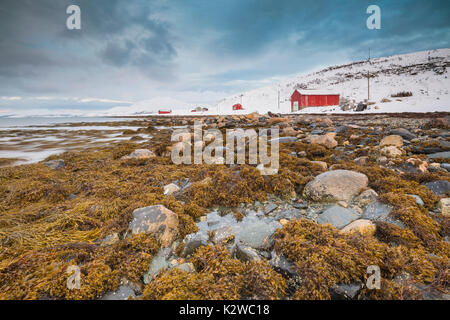 Typisch norwegische warmes und gemütliches Haus am See an einem Fjord in Troms County, Norwegen. Die Sonne tief über dem Horizont und der Himmel ist bewölkt Stockfoto