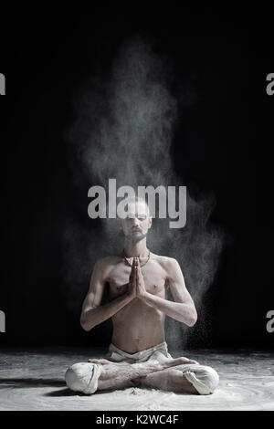 Ein Yoga Lehrer sitzt in einem sukhasana auf schwarzem Hintergrund. Stockfoto