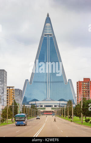 Straße mit Bus und Menschen in der Innenstadt von Pyongyang, Nordkorea mit dem Wahrzeichen Ryugyong Hotel im Hintergrund. Stockfoto