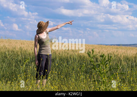 Kaukasische Frau mit Hut zeigen mit dem Finger auf den blauen Himmel in ein Feld. Stockfoto