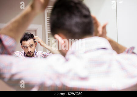Junger Mann mit Friseur und Kosmetik bei Haar Pflege. Er trägt Shirt mit Schachbrettmuster. Er berührt seine schwarzen Haare. Stockfoto