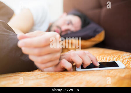 Mann lyng im Bett Ausschalten des Alarms Stockfoto