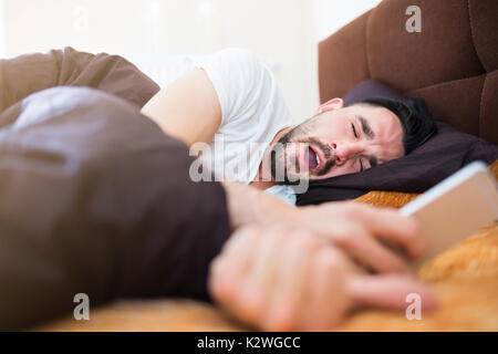 Mann lesen SMS-Nachricht auf sein Smartphone im Bett und Gähnen Stockfoto