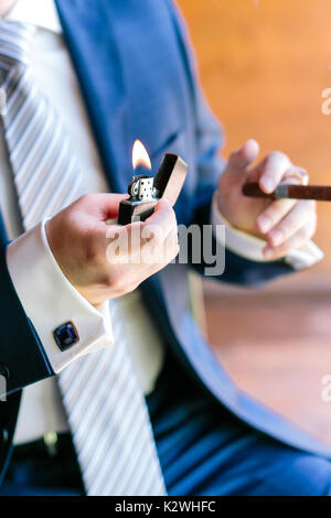 Erfolg, Rauchen, Feier Konzept. Bestens präparierte Arme der kaukasischen Mann, in Blau mode Kostüm gemacht mit wunderbaren Manschettenknöpfe zu messen gekleidet, wobei Hoffmann und cheroot Stockfoto