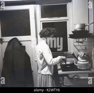 1960, historische, Bild einer Dame kochen auf ihren Selbst auf einem Gasherd in einem kleinen und einfachen Küche auf der Rückseite eines Reihenhauses, England, UK. Stockfoto