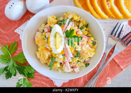 Salat aus Orange, Krabben Fleisch, Eier, Getreide mit Joghurt in einer weißen Schüssel auf einem Tuch Hintergrund serviert. Einfaches Essen. Gesunde Ernährung Konzept. Stockfoto