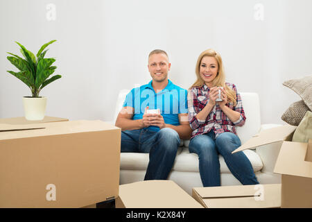 Glückliches junges Paar auf der Couch trinken Kaffee im neuen Haus Stockfoto